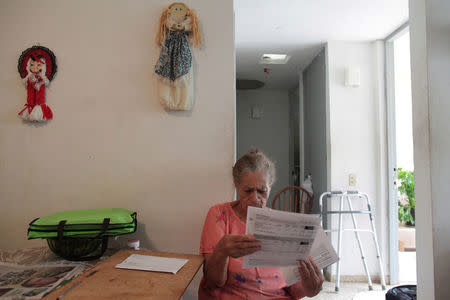 Juanita Gomez Cruz, who is the sole caretaker for her husband and her adult son and both of whom are disabled, reads a bill at her home in San Juan, Puerto Rico, November 15, 2016. REUTERS/Alvin Baez
