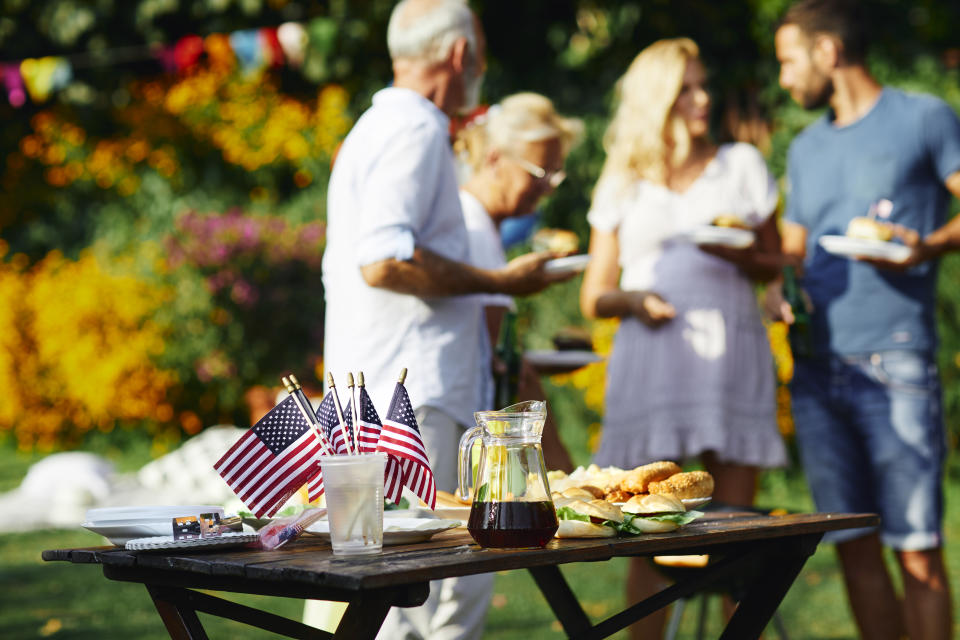 Multi-generation family on picnic in back yard celebrating 4th of July - Independence Day. Selective focus on food and drink with american flags on the table.