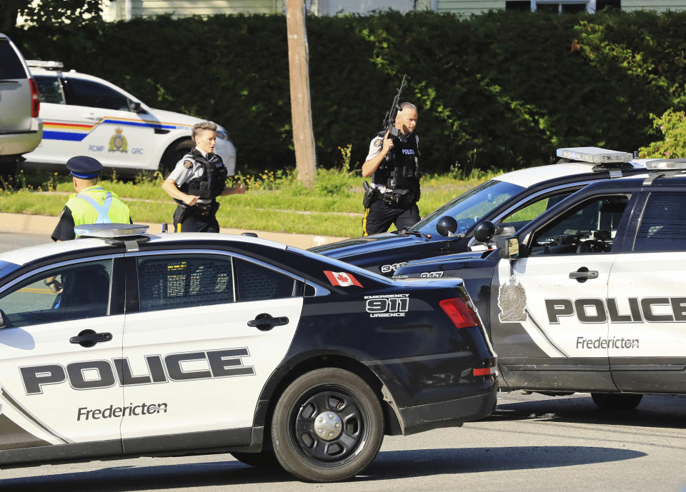Police and RCMP officers survey the area of a shooting in Fredericton, New Brunswick, Canada on Friday, Aug. 10, 2018. Fredericton police say two officers were among four people who died in a shooting Friday in a residential area on the city's north side. One person was in custody, they said, and there was no further threat to the public. (Keith Minchin/The Canadian Press via AP)