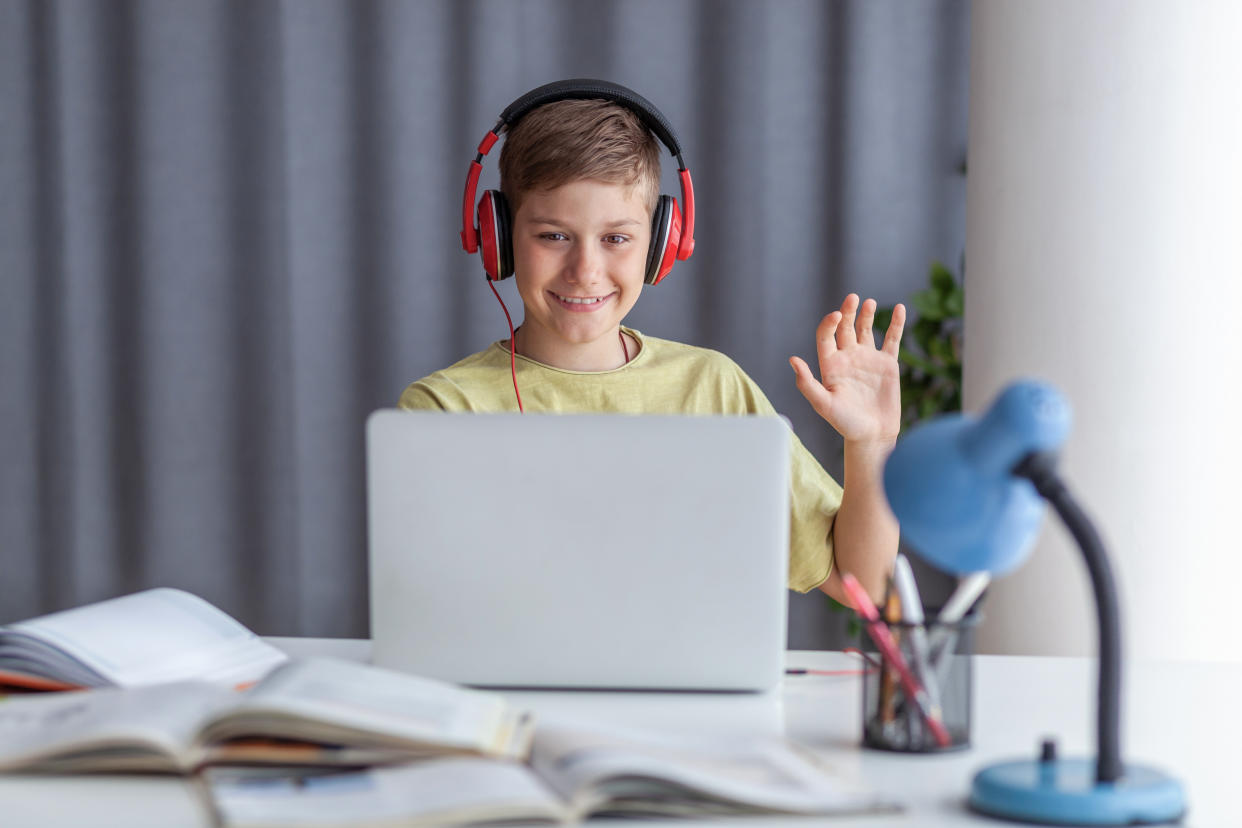 Happy elementary student waving to someone while having an online class over computer at home. Copy space.