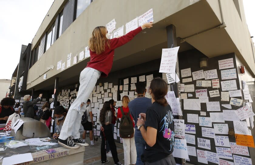 LOS ANGELES, CA - OCTOBER 22: USC junior student Bianca Ventola attaches a sign to the Sigma Nu fraternity house near the USC campus. USC officials have placed the Sigma Nu fraternity chapter on interim suspension following allegations that women were drugged and sexually assaulted at the fraternity house. In a crime alert issued Thursday, the USC Department of Public Safety said campus officials received "a report of sexual assault" at the Sigma Nu fraternity house locate at 660 W. 28th St. "The university also has received reports of drugs being placed into drinks during a party at the same fraternity house, leading to possible drug-facilitated sexual assaults," according to the alert. USC on Friday, Oct. 22, 2021 in Los Angeles, CA. (Al Seib / Los Angeles Times).