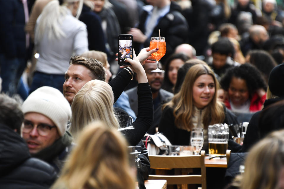 A woman takes a phone picture of her drink in Soho, London, on the day some of England's coronavirus lockdown restrictions were eased by the British government, Monday, April 12, 2021. People across England can get their hair cut, eat and drink outside at restaurants and browse for clothes, books and other "non-essential" items as shops and gyms reopened Monday after months of lockdown. (AP Photo/Alberto Pezzali)