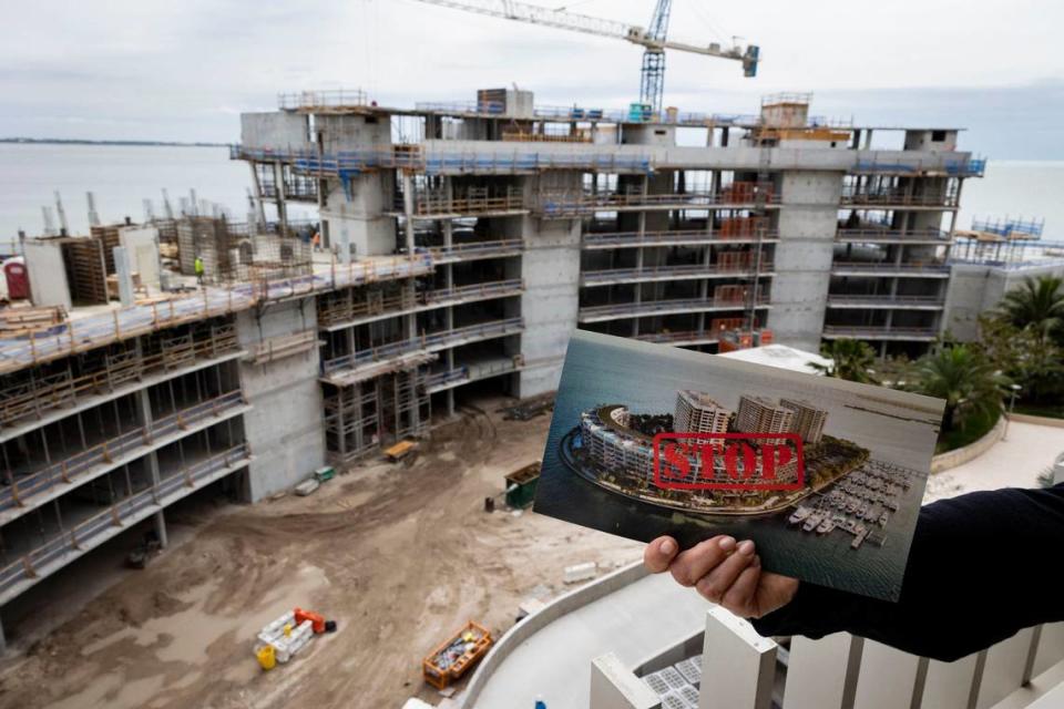 Un habitante de Grove Isle que ha estado luchando contra el nuevo edificio de condominios en construcción sosteniendo un panfleto mientras está de pie en un octavo piso del Edificio 3.