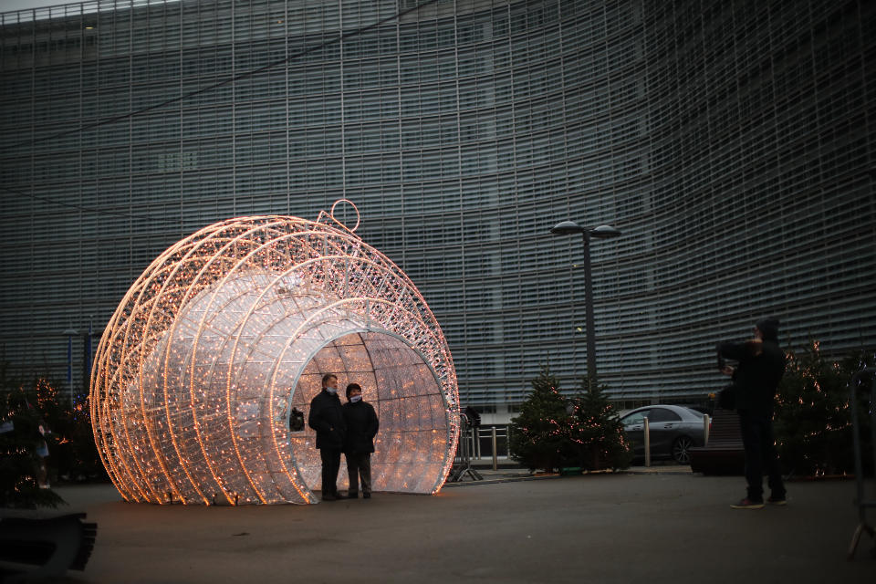 Passers by pose for a photograph next to Christmas decorations placed outside the European Commission headquarters in Brussels, Saturday, Dec. 12, 2020. British Prime Minister Boris Johnson and European Commission President Ursula von der Leyen have set a Sunday deadline to decide whether to keep talking or prepare all-out for a no-deal break. (AP Photo/Francisco Seco)