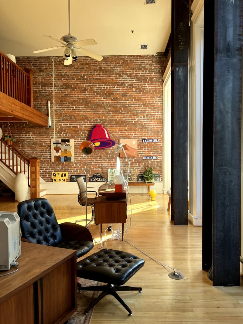 Black leather chair and ottoman and desks seen in loft with brick wall and ceiling fan.