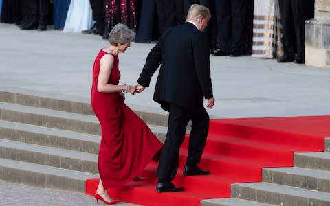Prime Minister Theresa May takes the hand of President Donald Trump as they walk up red-carpeted steps to enter Blenheim Palace - Credit: EPA