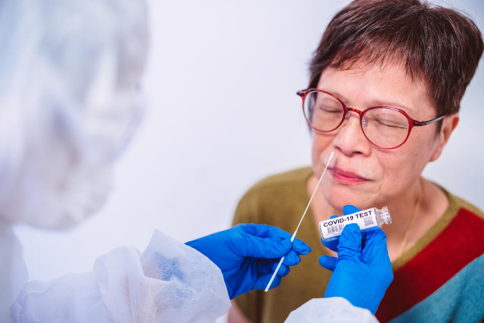 Doctor in protective gloves & workwear holding Testing Kit for the coronavirus test. The doctor is collecting nasal sample for a senior woman with a sampling swab.