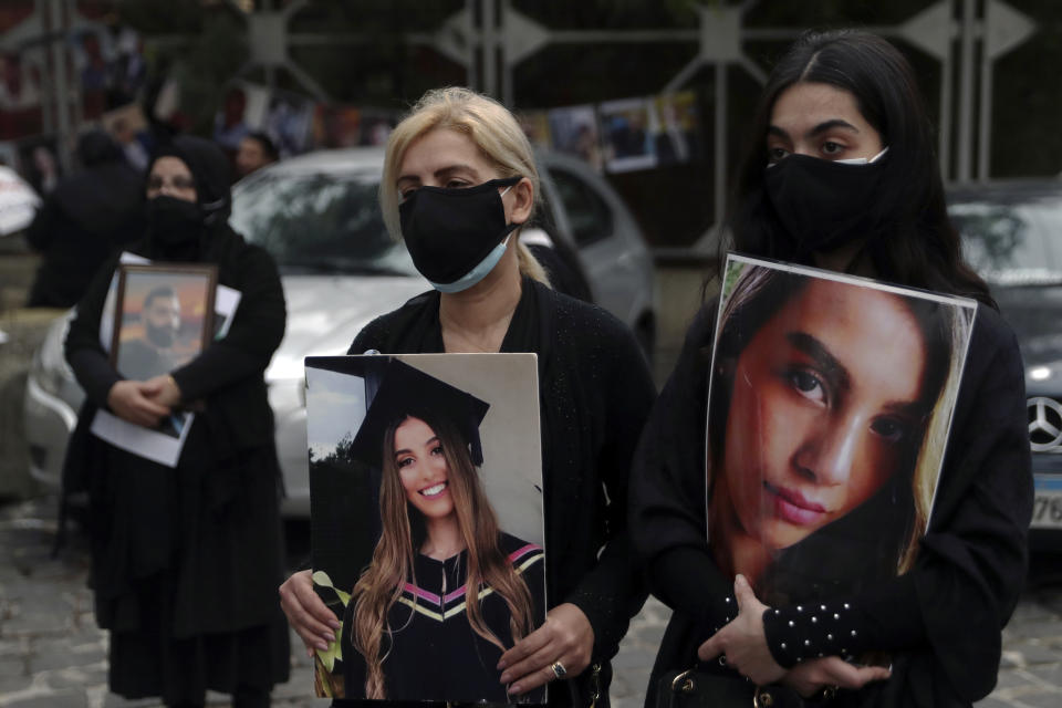 Relatives of the victims of the Aug. 4, 2020 Beirut port explosion hold portraits of their loved ones who were killed, Thursday, Feb. 4, 2021 in Beirut, Lebanon. The vigil at the seaport main entrance, marked six months since the blast that killed more than 200 people and injured thousands. The Arabic words on poster read "Who brought nitrates and for who? We have a right to know." (AP Photo/Bilal Hussein)