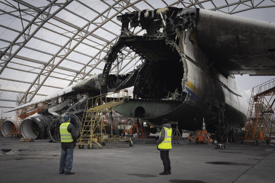 Airport workers look at the gutted remains of the Antonov An-225, the world's biggest cargo aircraft, destroyed during fighting between Russian and Ukrainian forces, at the Antonov airport in Hostomel, on the outskirts of Kyiv, Ukraine, Saturday, April 1, 2023. (AP Photo/Efrem Lukatsky)
