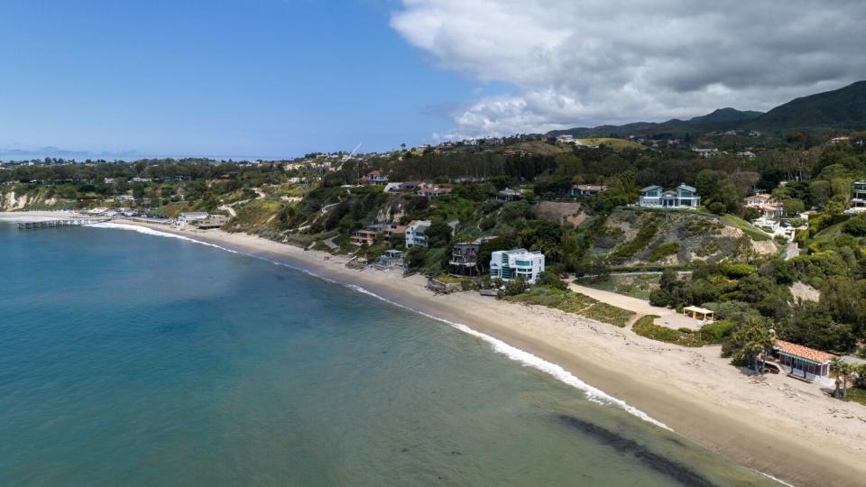 Luxury homes and green hills rise along a stretch of coastline.