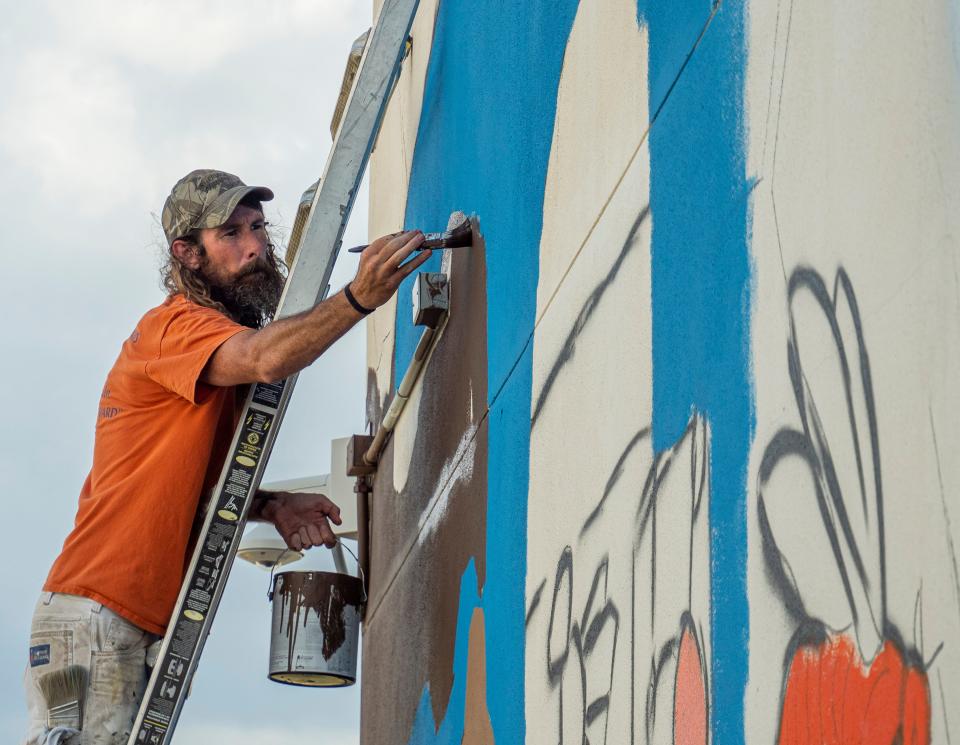 Muralist Andrew Raymond paints a section of a mural at Leesburg High School in Leesburg on Tuesday, May 24, 2022. [PAUL RYAN / CORRESPONDENT]