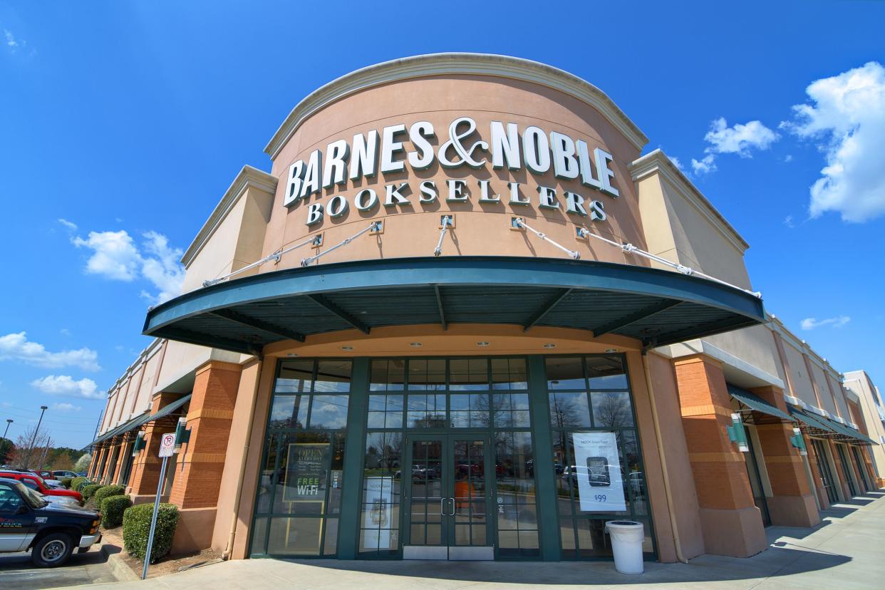 Front exterior and doors of Barnes & Noble, Athens, Georgia, fisheye lens, cars parked on the left, sidewalk on the right, on a sunny day during winter with a blue sky with white clouds in the background