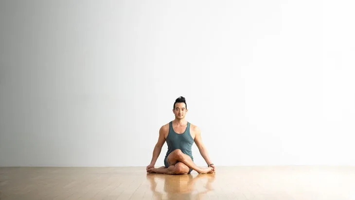 Hiro Landazuri sits with his legs crossed in Gomukhasana variation, Cow Face Pose