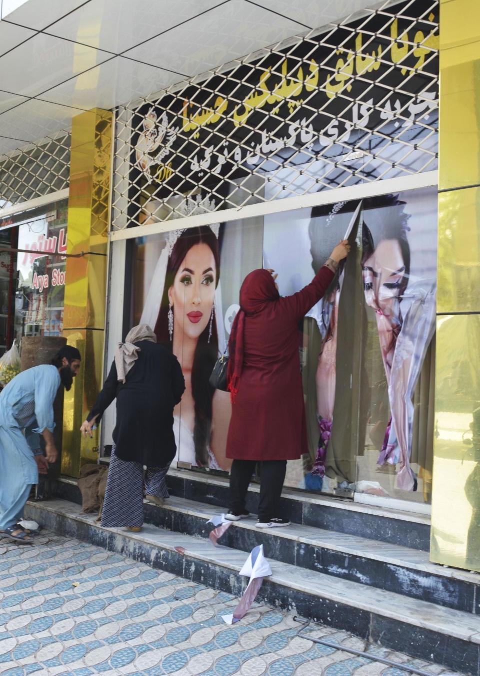 Workers at a beauty salon strip large photos of women off the wall in Kabul