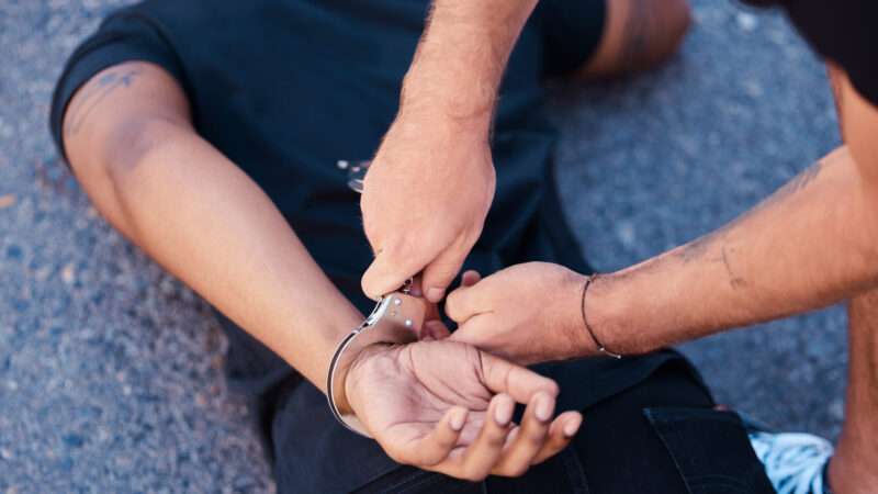 Police officer handcuffing a suspect who is facedown on the ground.