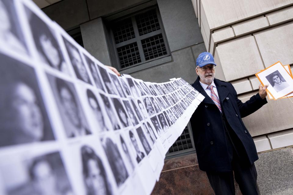 Paul Hudson of Sarasota, Fla., holds up a photo of his daughter Melina who was killed at 16 years old along with the photos of almost a hundred other victims of the bombing of Pan Am Flight 103 over Lockerbie, Scotland, as he speaks to members of the media in front of the federal courthouse in Washington, Monday, Dec. 12, 2022. The Justice Department says a Libyan intelligence official, Abu Agila Mohammad Mas'ud Kheir Al-Marimi, accused of making the bomb that brought down Pan Am Flight 103 over Lockerbie, Scotland, in 1988 in an international act of terrorism has been taken into U.S. custody and will face federal charges in Washington. (AP Photo/Andrew Harnik)