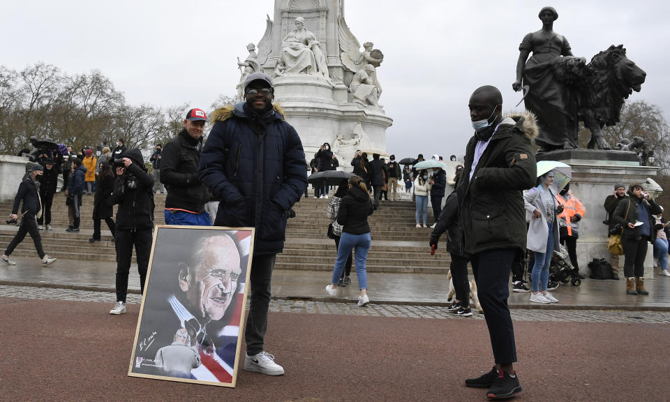 A man stands with an artwork depicting Britain's Prince Philip outside Buckingham Palace in London, a day after the death of Britain's Prince Philip, Saturday, April 10, 2021. Britain's Prince Philip, the irascible and tough-minded husband of Queen Elizabeth II who spent more than seven decades supporting his wife in a role that mostly defined his life, died on Friday. (AP Photo/Alberto Pezzali)