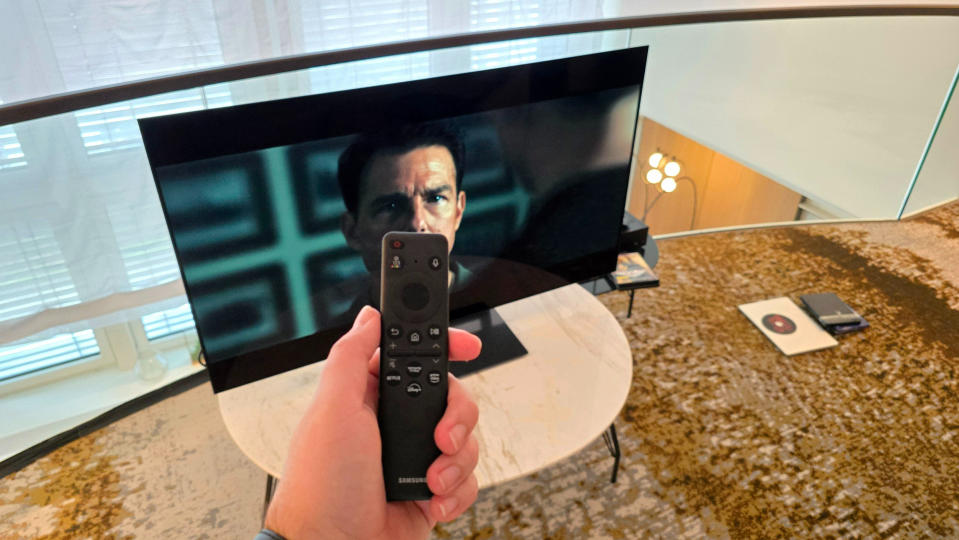 Samsung S90D 48-inch TV on a marble table with Top Gun Maverick playing on screen and the TV remote in the foreground