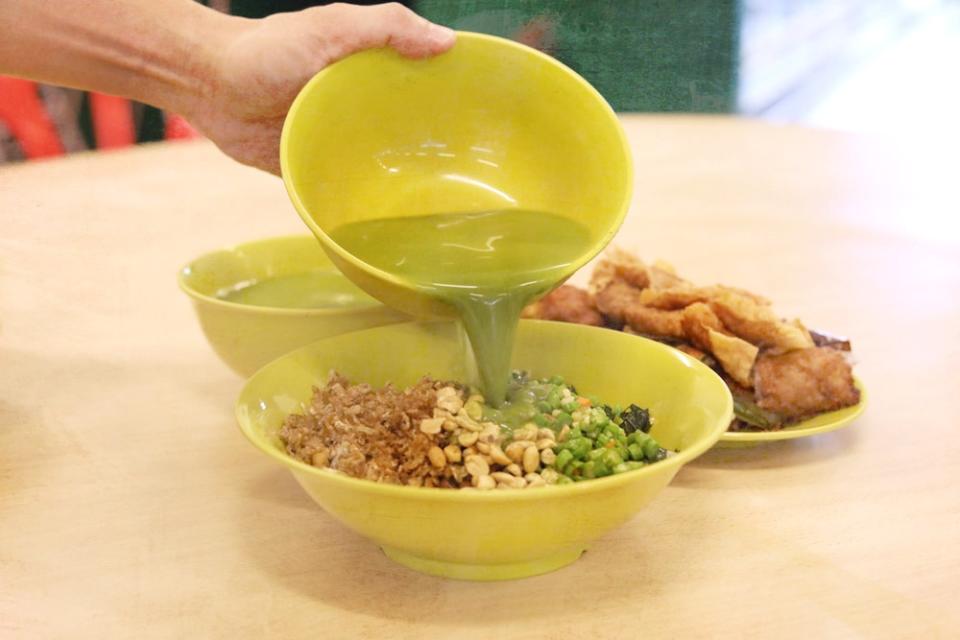 Pour the hot green broth into the bowl of rice and chopped ingredients for a complete 'lei cha'.