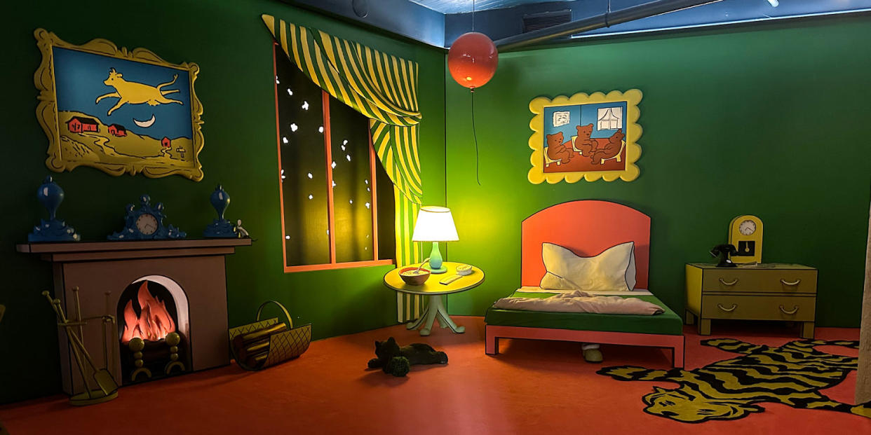 A dimly lit cartoon-like bedroom with a fireplace, bed, window, tiger rug, and balloon on the ceiling (Mara Stein / NBC News)