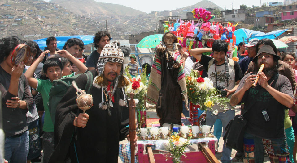 In this Nov. 1, 2012 photo, Shaman Paul Naveda, front center left, calls the spirits with a maraca as Fernando Naveda, right, plays the flute during the procession of Santa Muerte during the Day of the Dead festival at the Cemetery of Nueva Esperanza in Villa Maria del Triunfo in Lima, Peru. Claudio Ajayu, far left with tambourine, and Adrian Abel Naveda Cabrera, green shirt, look on. (AP Photo/Jody Kurash)