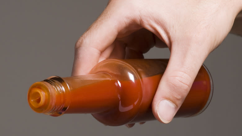 A hand holding an open bottle of red hot sauce