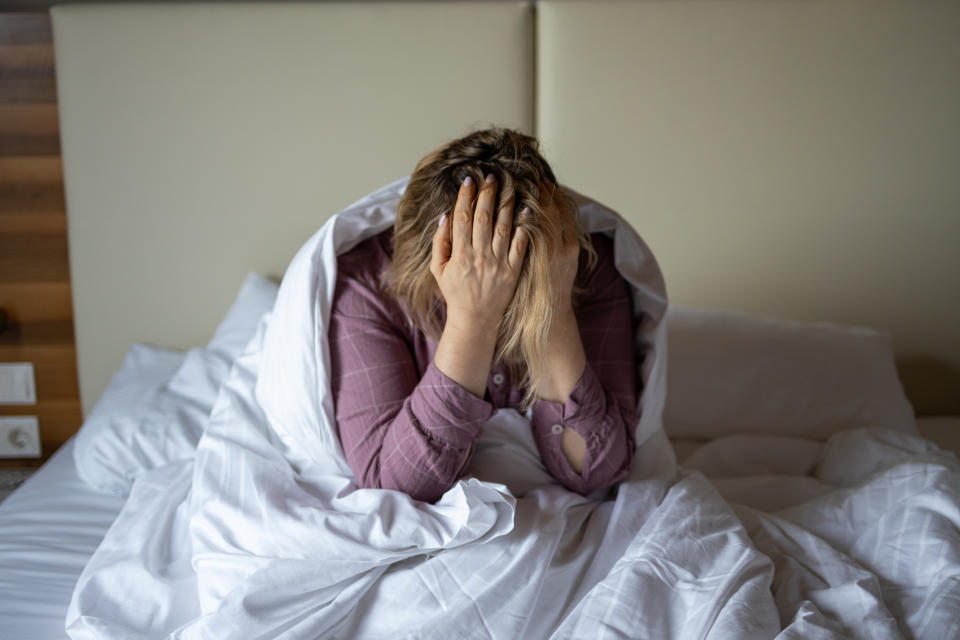 Person sitting on a bed with their head in their hands, showing signs of distress or frustration