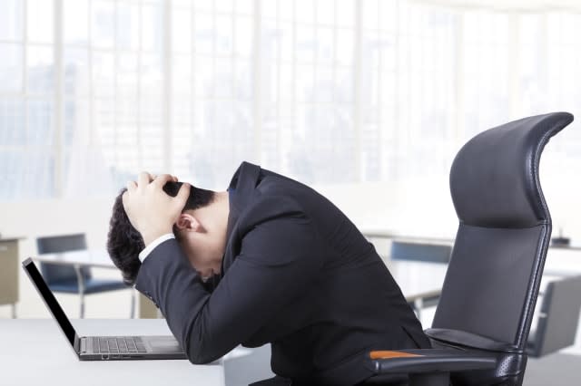 Stressful entrepreneur sitting in the office chair with a laptop on the table and holding his head