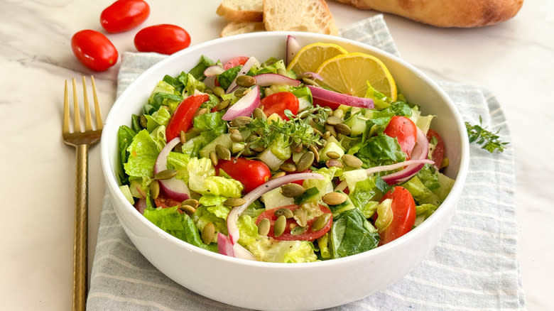 serving bowl of green salad with tomatoes and lemon
