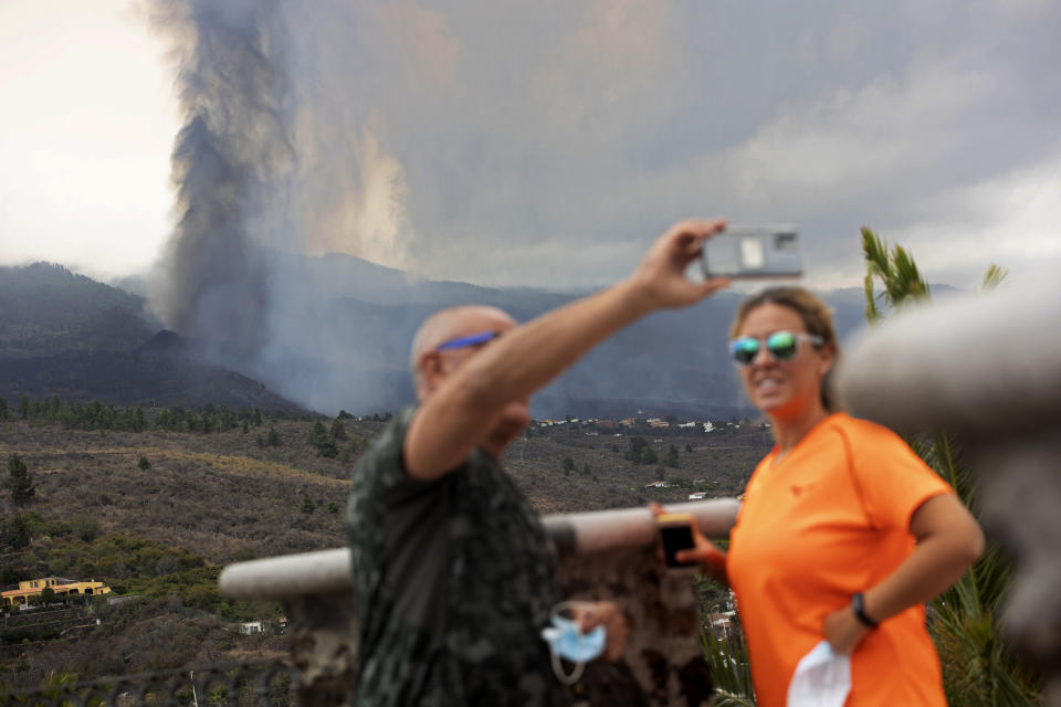 A couple take selfies in front of the eruption of a volcano near El Paso on the island of La Palma in the Canaries, Spain, Monday, Sept. 20, 2021. Lava continues to flow slowly from a volcano that erupted in Spain's Canary Islands off northwest Africa. Officials say they are not expecting any other eruption and no lives are currently in danger. (AP Photo/Gerardo Ojeda)