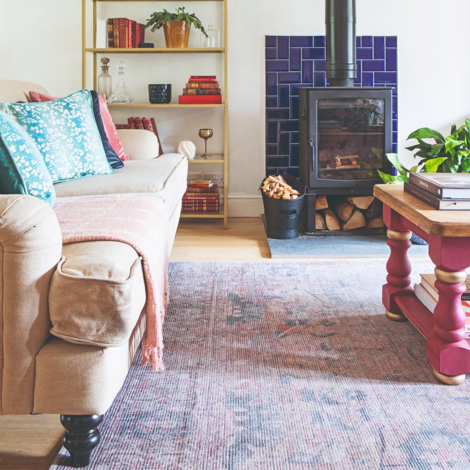 A light pink traditional sofa postioned on a patterned purple rug with a wooden coffee table with pink-painted legs