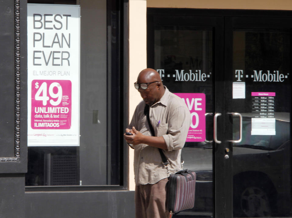 A man checks his mobile phone as he walks past a T-Mobile store in downtown Los Angeles, California August 31, 2011. The Obama administration on Wednesday fired a legal broadside to block AT&T Inc's $39 billion acquisition of T-Mobile, launching its biggest challenge yet to a takeover and dealing the carrier a potentially costly blow.         REUTERS/Fred Prouser  (UNITED STATES - Tags: BUSINESS TELECOMS)