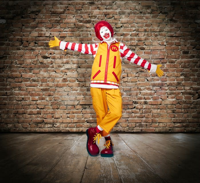 A costumed Ronald McDonald in front of a brick wall.