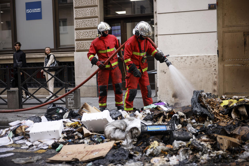 Firemen controlling the remains of a garbage fire from last night protests against the retirement bill in Paris, Friday, March 24, 2023. French President Macron's office says state visit by Britain's King Charles III is postponed amid mass strikes and protests. (AP Photo/Thomas Padilla)