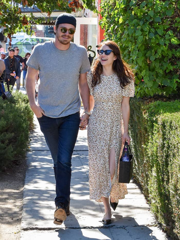 Garret and Emma walking down the sidewalk hand-in-hand and smiling during happier times