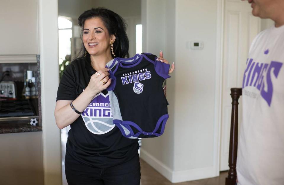 Sue Awabdeh holds up baby Sacramento Kings outfits that await her first grandchild Tuesday, April 11, 2023, at her home in El Dorado Hills.