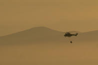 As smoke engulfs the South African city of Cape town, a South African Military helicopter ferries water used to control a massive fire spreading on the slopes of Table Mountain Tuesday, April 20, 2021. (AP Photo/Jerome Delay)