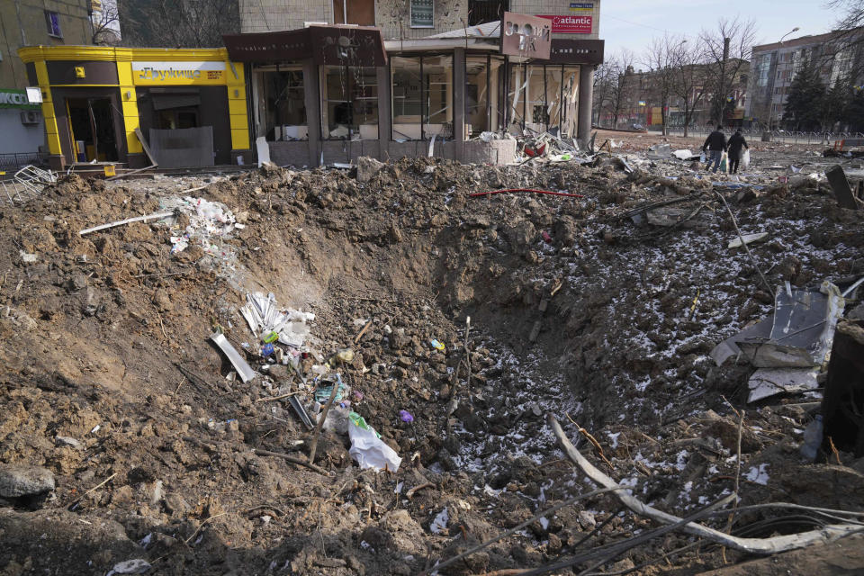 FILE - People walk past a crater from the explosion in Mira Avenue (Avenue of Peace) in Mariupol, Ukraine, Sunday, March 13, 2022. With its aspirations for a quick victory dashed by a stiff Ukrainian resistance, Russia has increasingly focused on grinding down Ukraine’s military in the east in the hope of forcing Kyiv into surrendering part of the country’s eastern territory to end the war. If Russia succeeds in encircling and destroying the Ukrainian forces in Donbas, the country’s industrial heartland, it could try to dictate its terms to Kyiv -- and possibly attempt to split the country in two. (AP Photo/Evgeniy Maloletka)