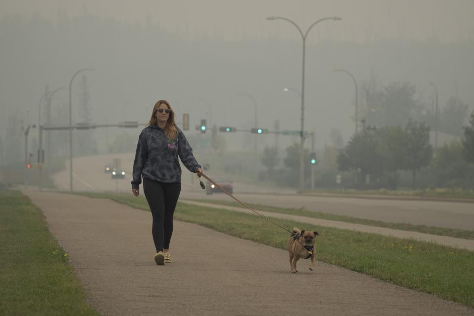 Brittnee McIsaac, a school teacher, walks her dog on a smoky day because of wildfires in Fort McMurray, Canada, on Saturday, Sep. 2, 2023. "It really takes a toll on the mental health; just how dreary it is every day," she said of the smoke. (AP Photo/Victor R. Caivano)