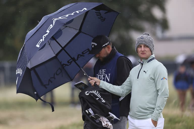 Al revés: Emiliano Grillo sostiene el paraguas para su caddie, que anota en la tarjeta; el chaqueño cayó en su rendimiento pero conserva expectativas grandes.