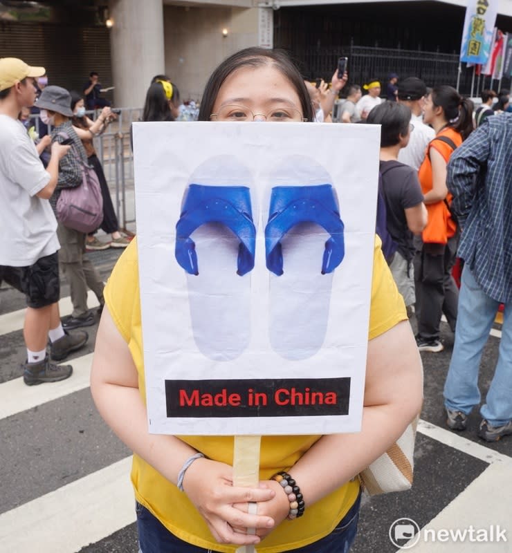 一位女性民眾拿著中國製的藍白拖鞋，表達對藍白兩黨的不滿。   圖：張良一/攝