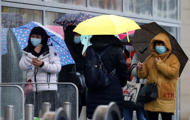 FILE PHOTO: People wearing face masks shelter under umbrellas outside a department store following the outbreak of the coronavirus disease (COVID-19) in Manchester