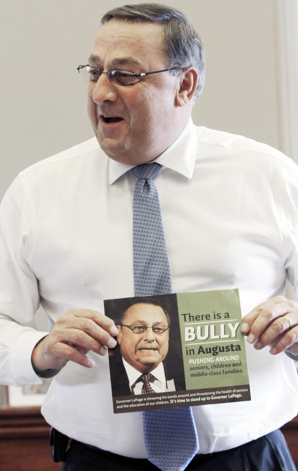 In this Friday, April 27, 2012 photo, Gov. Paul LePage talks about his sense of humor while holding a poster that reads "There is a bully in Augusta pushing around seniors, children and middle class families," during an interview with the Associated Press at his office at the State House in Augusta, Maine. Critics are putting pressure on LePage to apologize for referring to the Internal Revenue Service as "the new Gestapo" during his radio address Saturday, July 7, 2012. (AP Photo/Pat Wellenbach)