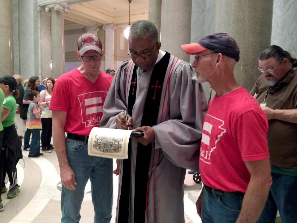 After marrying Allan Cox, 48, left, and Steve Thomas, 61, right, Judge Wendell Griffen, center, signs their marriage license in this Monday, May 12, 2014 photo in Little Rock, Ark. Lawyers for gay couples asked the state's highest court Tuesday, May 13, 2014 to let same-sex weddings continue amid a fight over Arkansas' gay marriage ban, while more than half the counties that had granted licenses to same-sex couples changed course. (AP Photo/Christina Huynh)