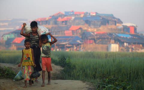  Rohingya refugee children carry supplies through Balukhali refugee camp near Cox's Bazar - Credit:  HANNAH MCKAY/Reuters