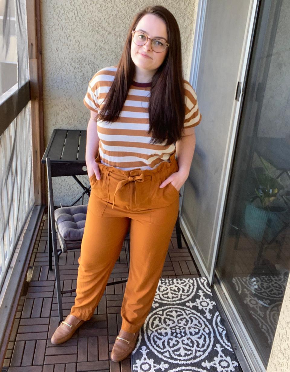 The writer on a balcony wearing a striped T-shirt, paper-bag pants, and loafers.