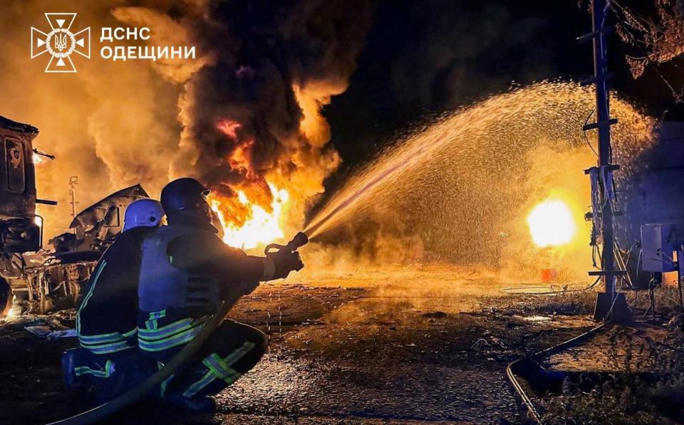 Members of emergency services use a water hose as flames and smoke rise