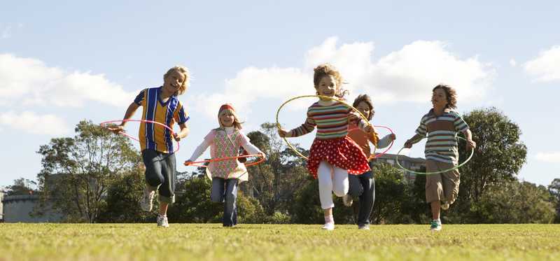 Five children with hula hoops in a grassy field on a sunny day.