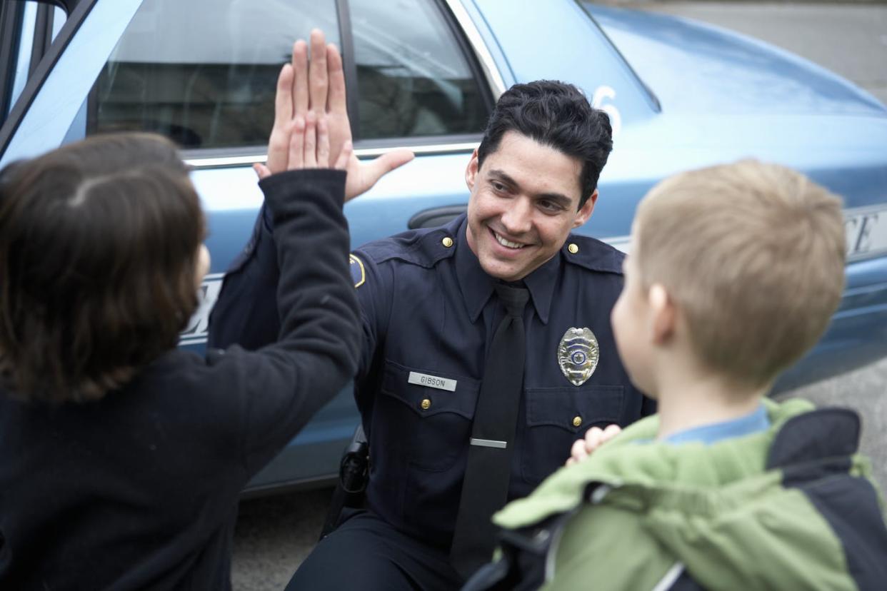 <span class="caption">For police officers, building trust is a key part of their job. </span> <span class="attribution"><a class="link " href="https://www.gettyimages.com/detail/photo/male-police-officer-high-fiving-a-young-boy-royalty-free-image/76536234" rel="nofollow noopener" target="_blank" data-ylk="slk:UpperCut via Getty Images;elm:context_link;itc:0;sec:content-canvas">UpperCut via Getty Images</a></span>
