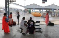 A municipal worker operates an "anti-smog gun" in India's capital as passengers are seen at a bus depot in New Delhi